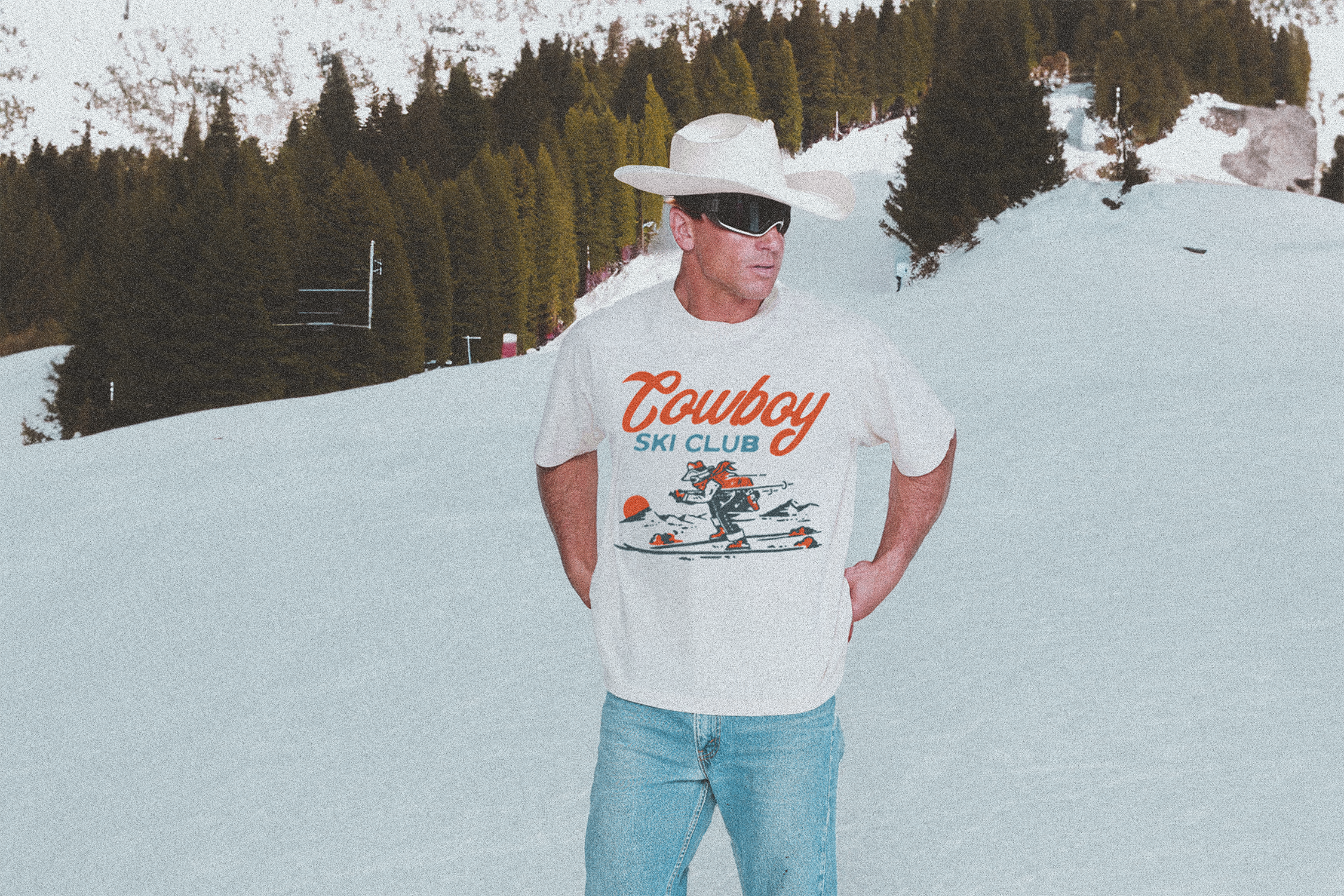 A man wearing a cowboy hat, ski googles, and the Resort Cowboy Tee in Ecru